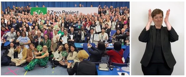 the screengrab shows a moment of the video where a large crowd can be seen posing for the traditional "family photo"; the sign interpreter is also visible in the split screen layout as a reference to the video's accessibility features