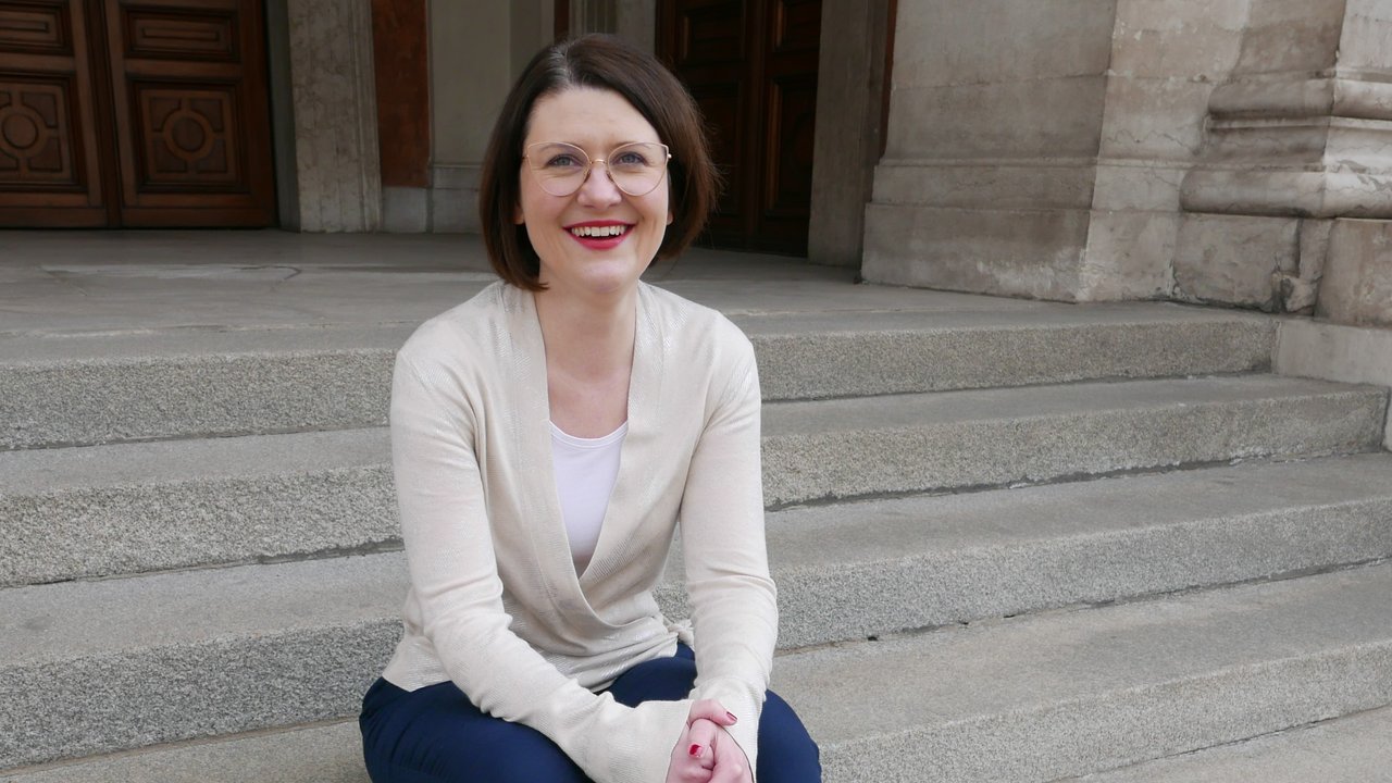 Anna Königseder sitting on the stairs of the House of Philanthropy, smiling and wearing a beige cardigan.