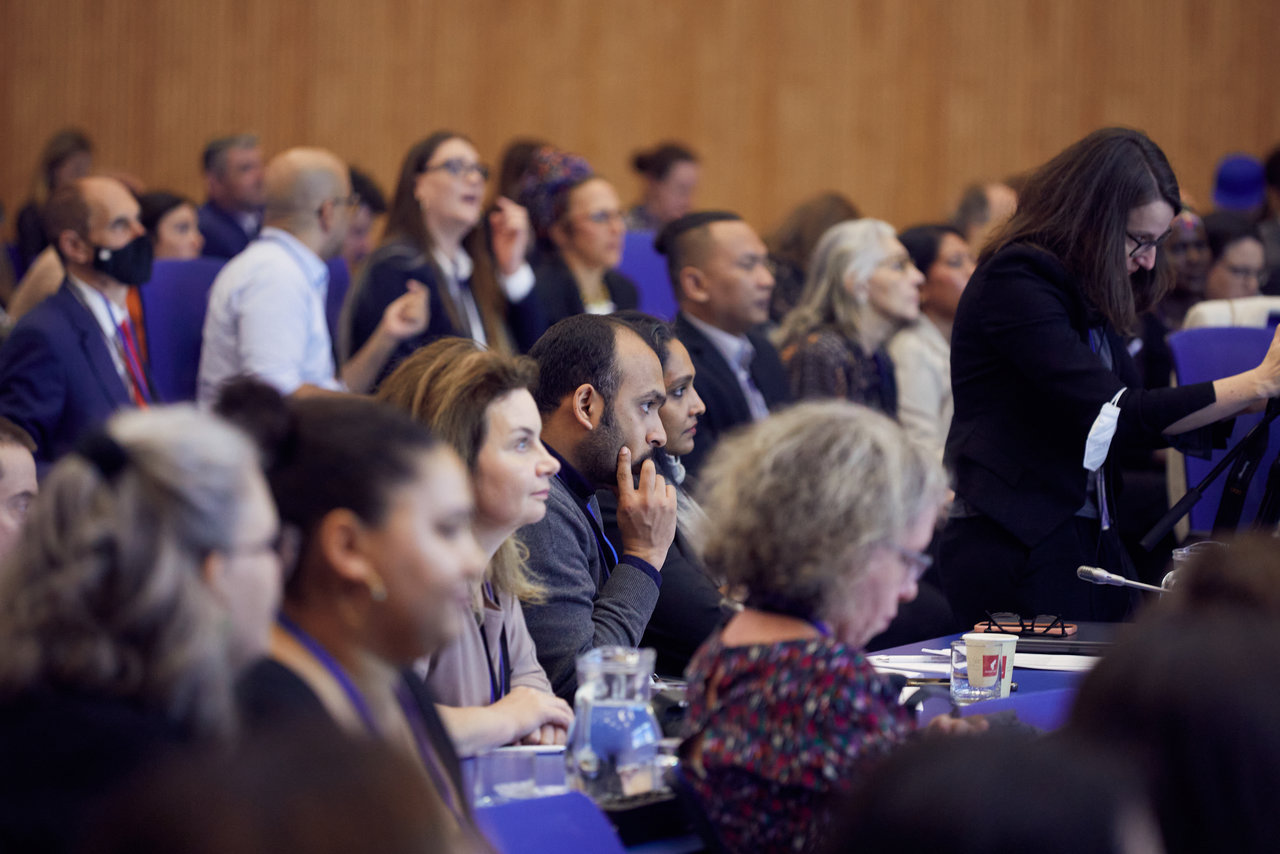 A plenary room filled with a large group of people who are attentively listening to someone outside the frame