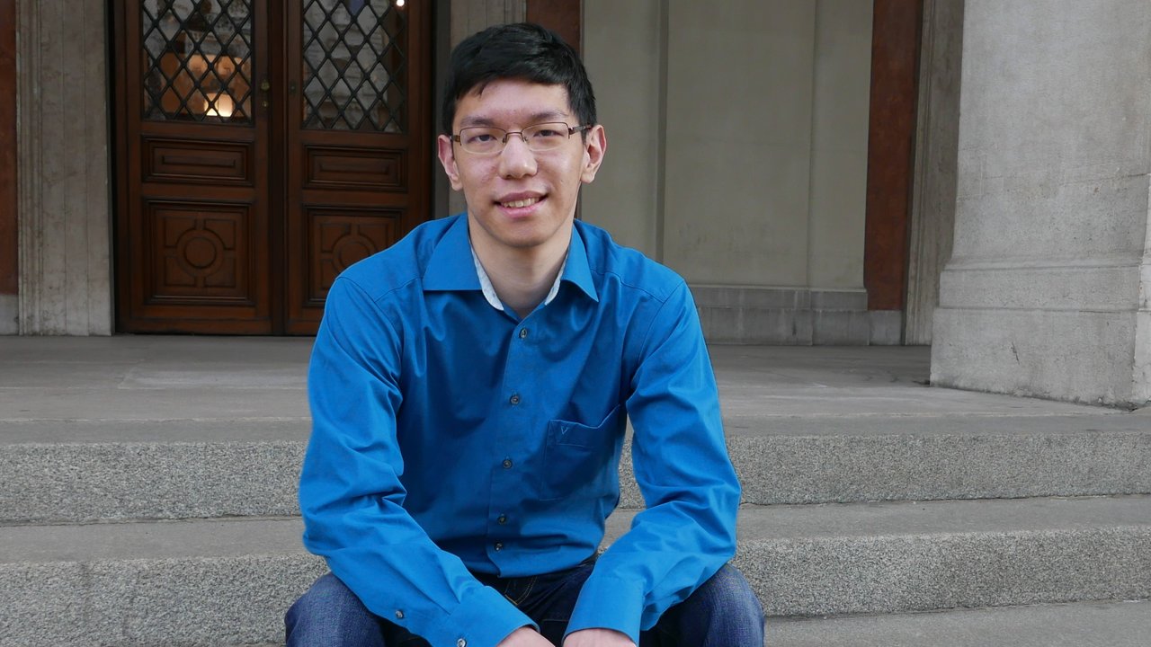 Xin Hu sitting on the entry stairs of the House of Philanthropy, smiling and wearing a blue shirt.