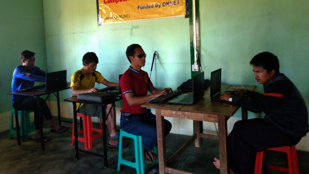 The photo shows four individuals engaged in a computer training session designed for the blind, as indicated by the banner in the background. They are sitting at tables with laptops, suggesting a learning environment that promotes digital literacy and inclusion for people with visual impairments. The setting appears to be a simple classroom, and the participants are focused on their tasks, embodying the spirit of determination and empowerment through education. This image is a testament to initiatives that support equal opportunities and accessibility in technology for all.