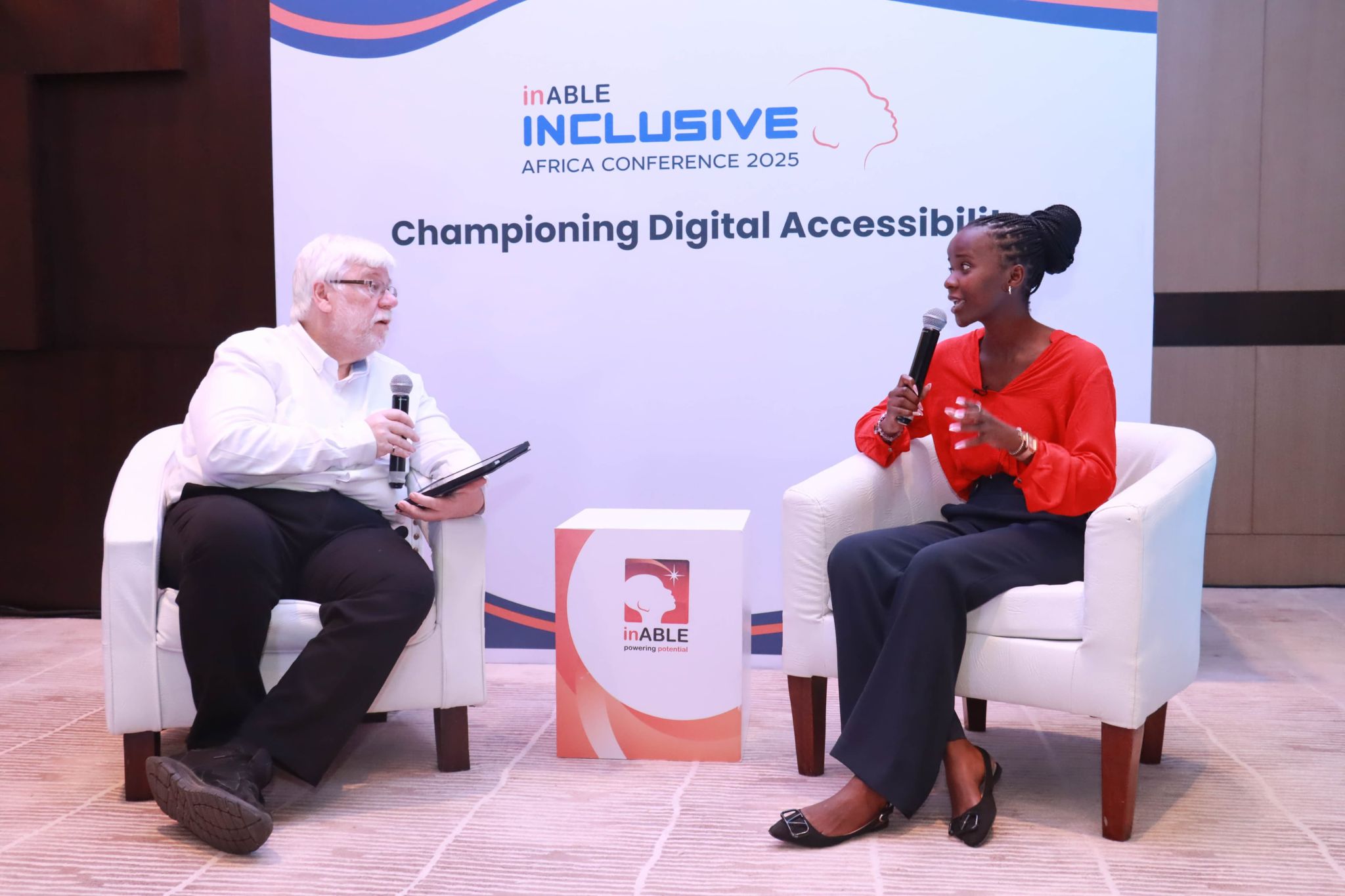 Two people seated and holding microphones engage in a discussion at the inABLE Inclusive Africa Conference 2025. The event focuses on digital accessibility.
