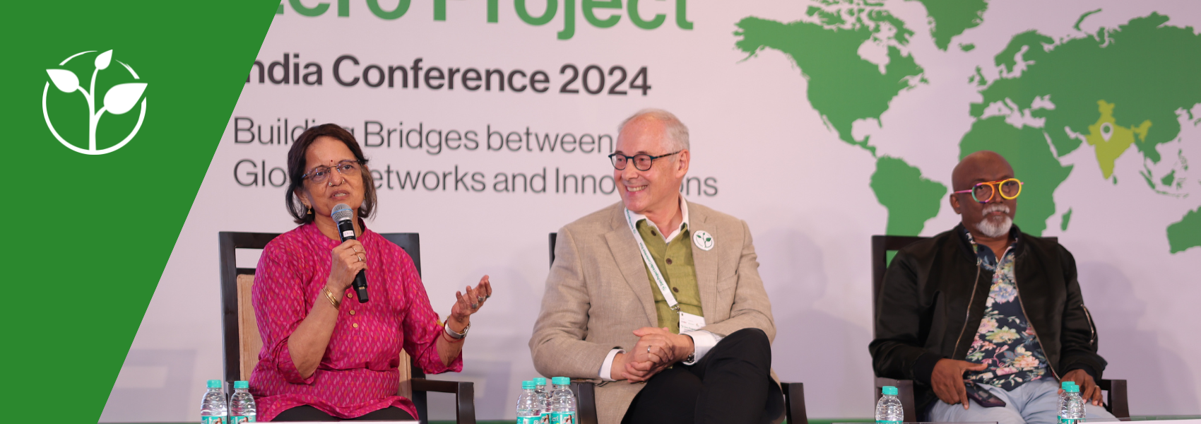 A photo from the ZeroConIndia24 panel on Inclusive Arts: Meera Shenoy talking into the microphone, addressing the audience; next to her is Martin Essl who looks at Meera smilingly. Next to Martin is the third panelist, Bose Krishnamachari who looks towards the audience. The three are seated in front of a big banner showing the conference name and a worldmap where India is highlighted.